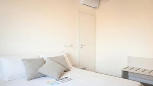 Quarto de hotel com cama, almofadas, mesa de cabeceira e ar condicionado fixado na parede.