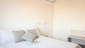 Una habitación de hotel con cama, almohadas, mesita de noche y aire acondicionado instalado en la pared.