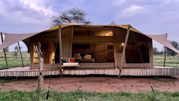 Une tente de safari dotée d’une terrasse en bois, d’un canapé et d’un coin repas.