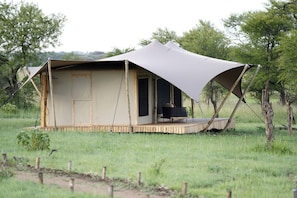 A safari tent with a covered porch and a single black chair.