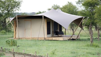 A safari tent with a covered porch and a single black chair.