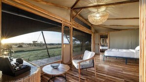 A tented accommodation with a bed, a seating area with a table, and a view of the outdoors.