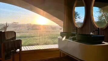 A room with a wooden floor, a wooden chair, a white cabinet with a sink, and two oval mirrors.