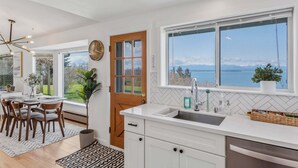 Una cocina moderna con un amplio ventanal, muebles blancos y vistas al mar.