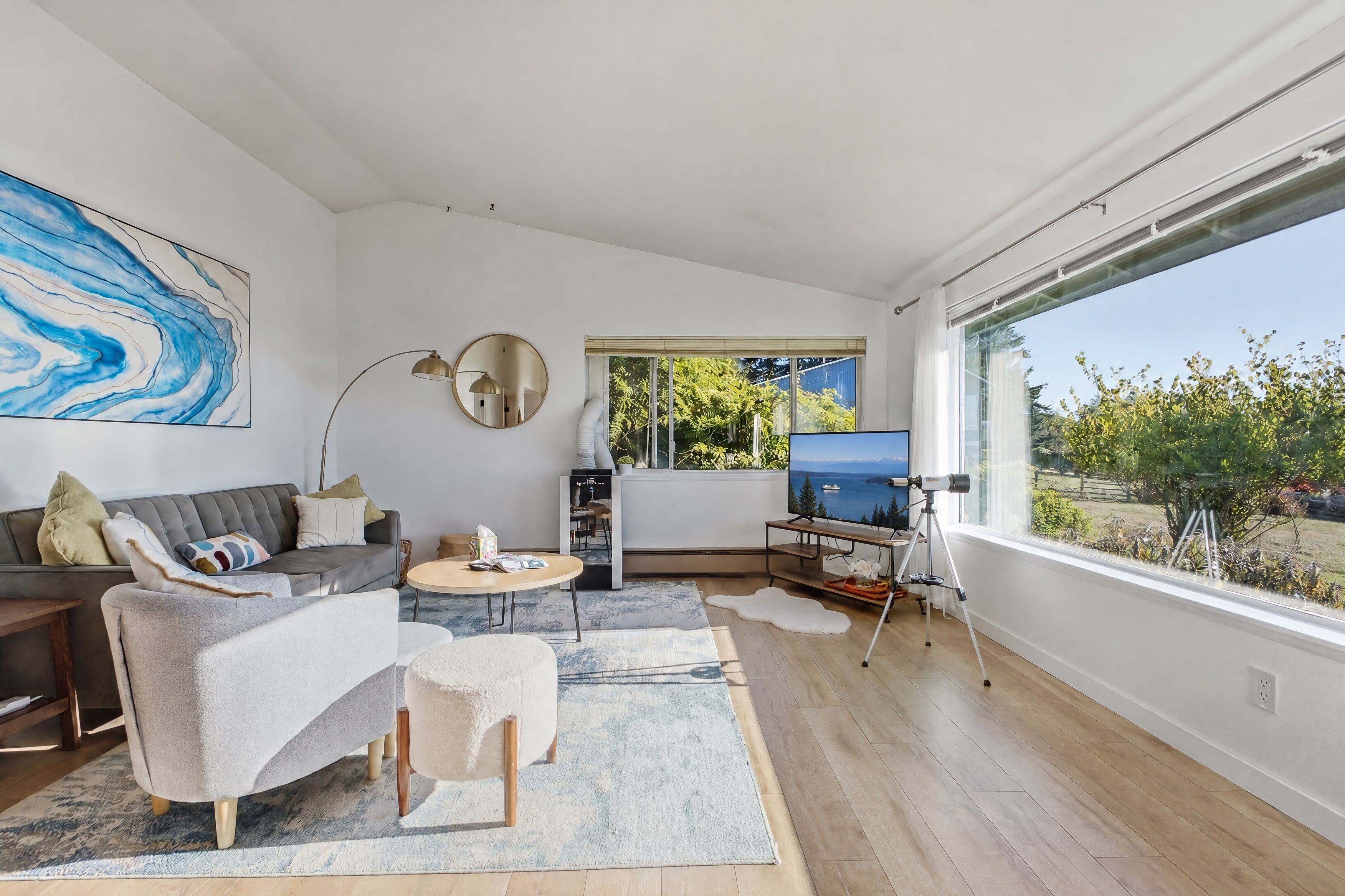 A modern living room with a sofa, armchair, coffee table, and a large window offering a view of greenery and a body of water.