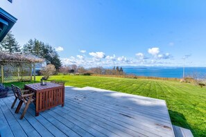 A deck with a table and chairs, overlooking a well-maintained lawn and a body of water.