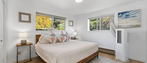 A bedroom with a bed, two bedside tables, a nightstand, a radiator, and a window with a view of trees.