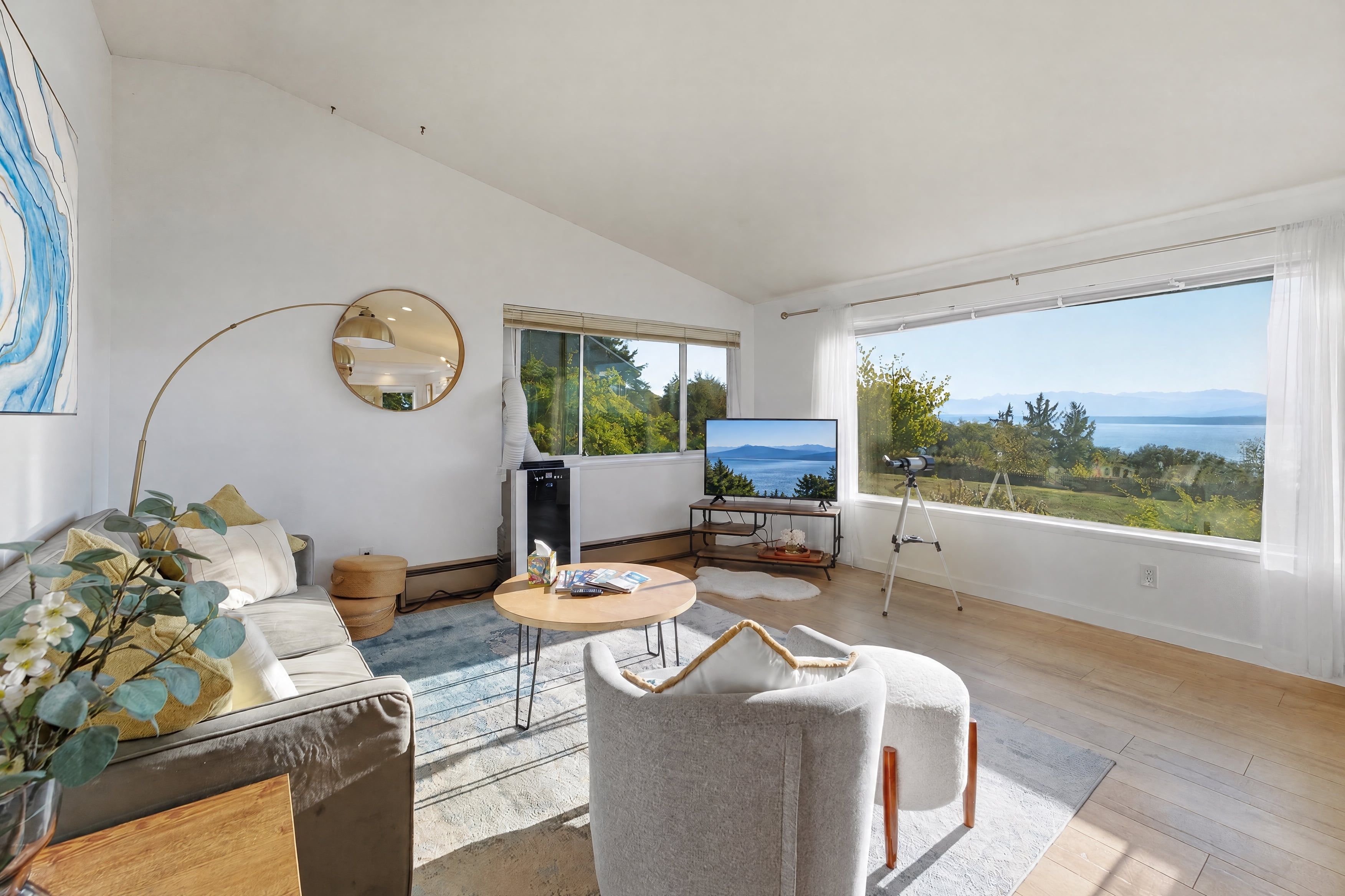 A modern living room with a large window, a sofa, a coffee table, and a television.