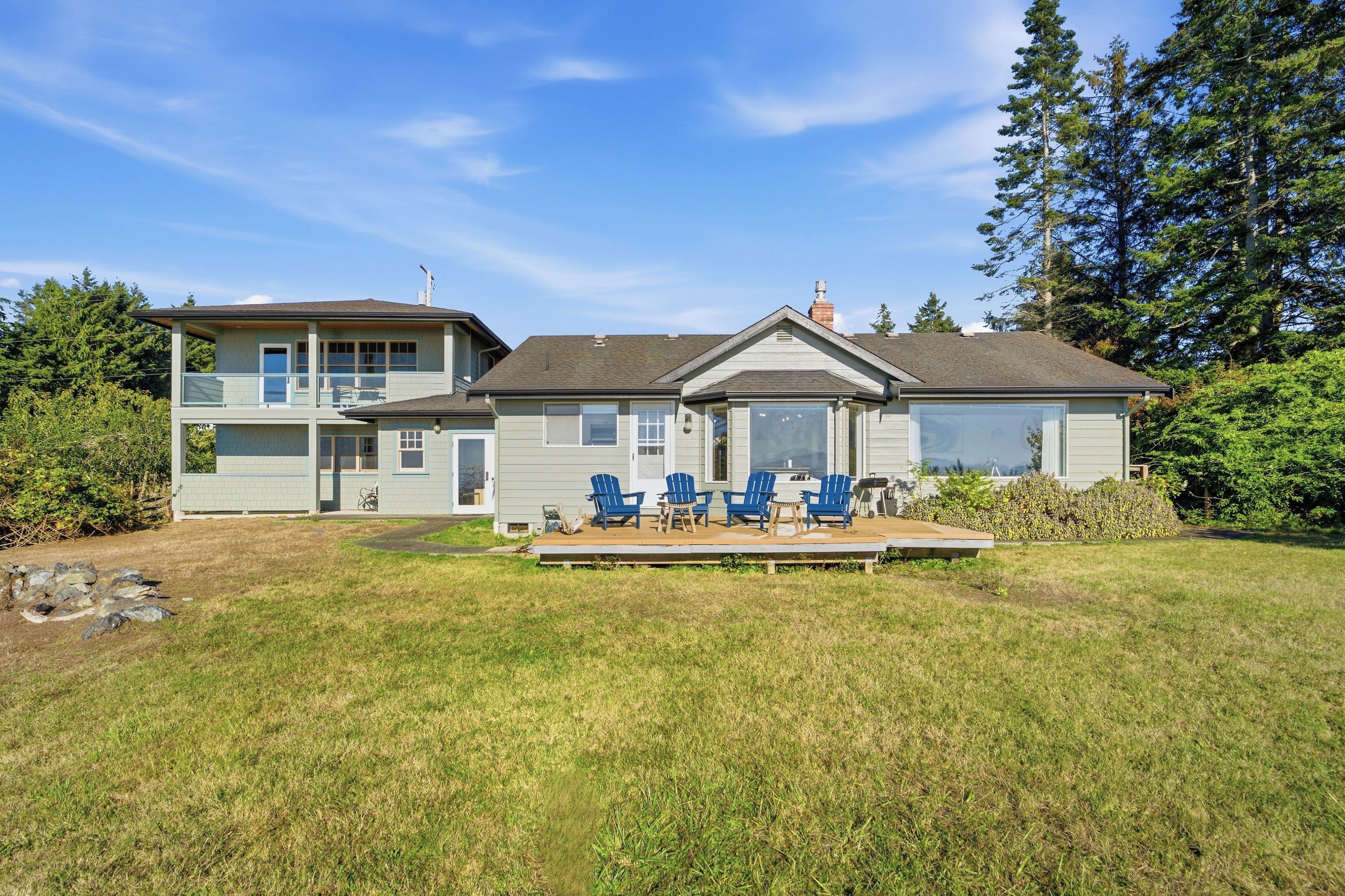 A two-story house with a deck, blue chairs, and a large window.
