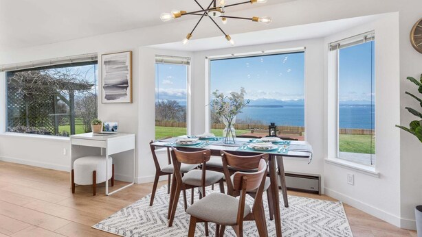 Un comedor con una mesa dispuesta para cuatro, un ordenador portátil sobre un escritorio y vistas al mar a través de amplios ventanales.