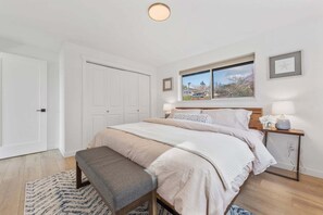 A bedroom with a bed, bench, bedside tables, and a window with a view.