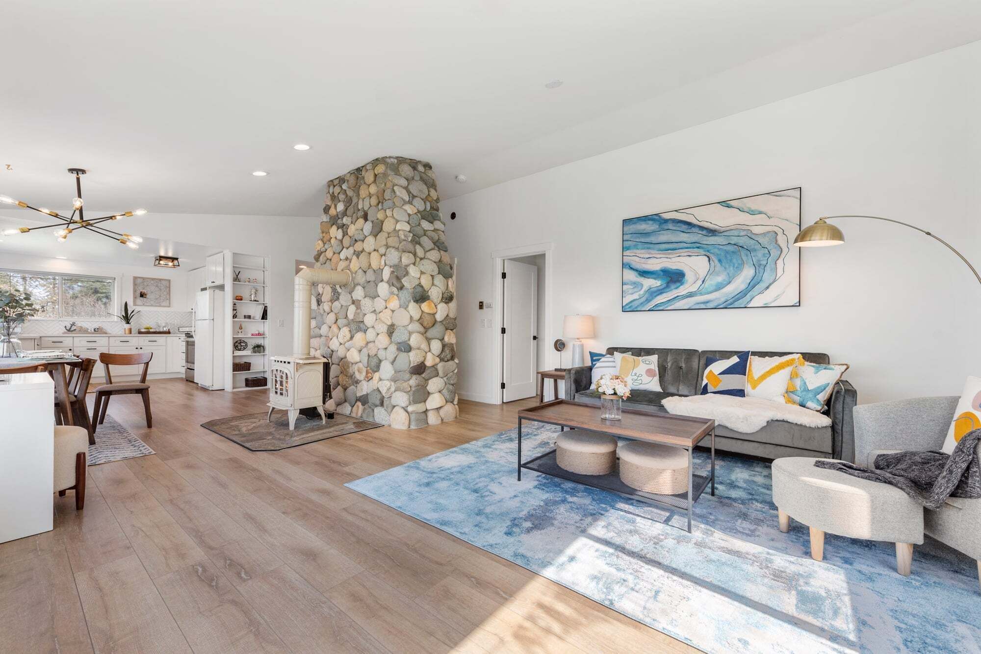 A modern living space with a stone fireplace, a dining area, and a seating area with a blue rug.