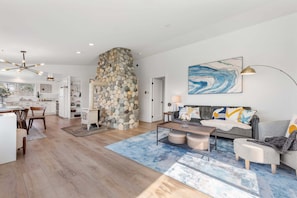A modern living space with a stone fireplace, a dining area, and a seating area with a blue rug. - Perch - 2BR Waterfront Bluff | Sunset Views | Free Parking (Coupeville)