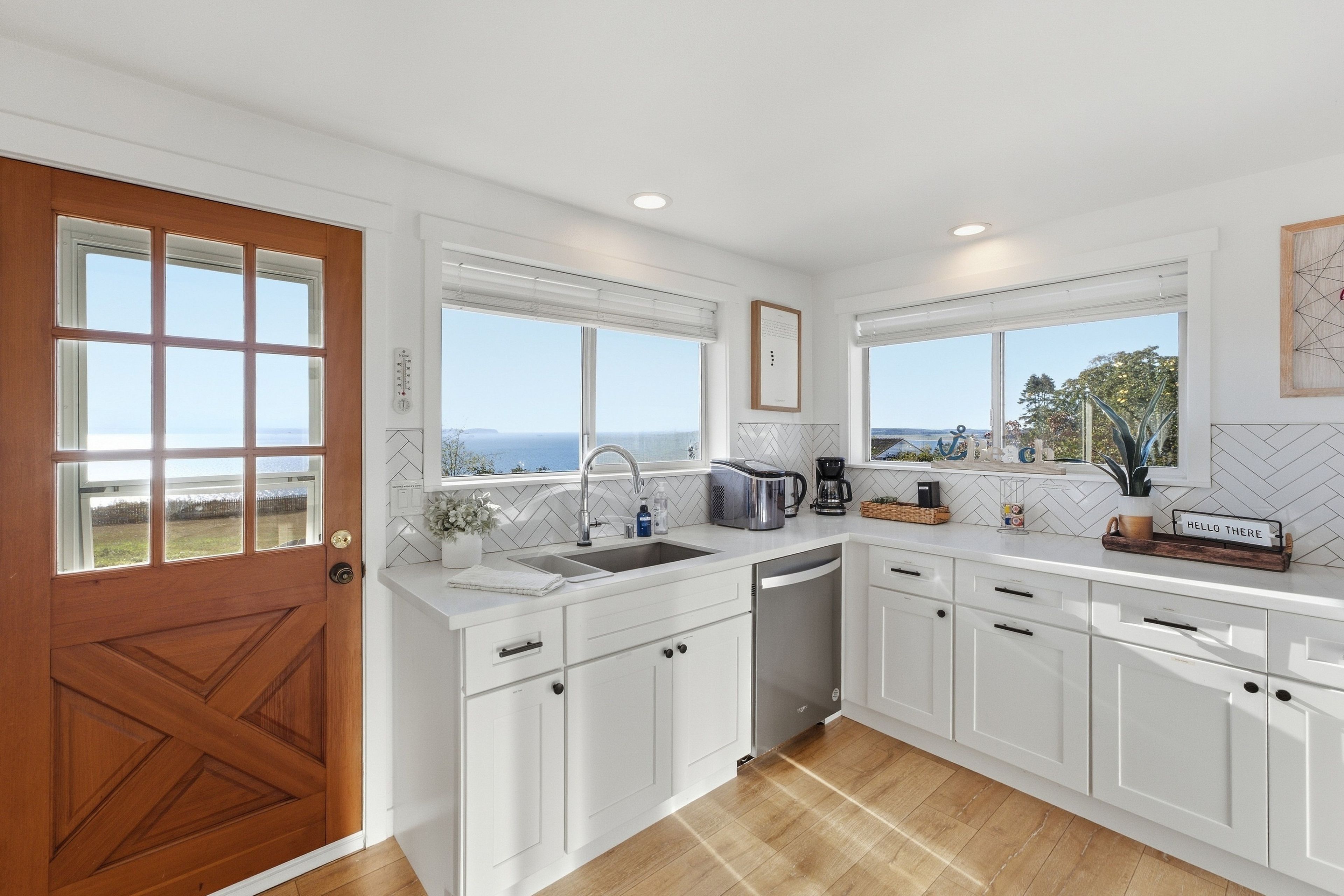 Une cuisine moderne avec des meubles blancs, une porte en bois et une vue sur la mer.