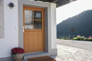 A wooden door with a glass panel, set in a stone wall with a mountain view in the background. - Chalet Suite "Happiness" (Berchtesgaden)