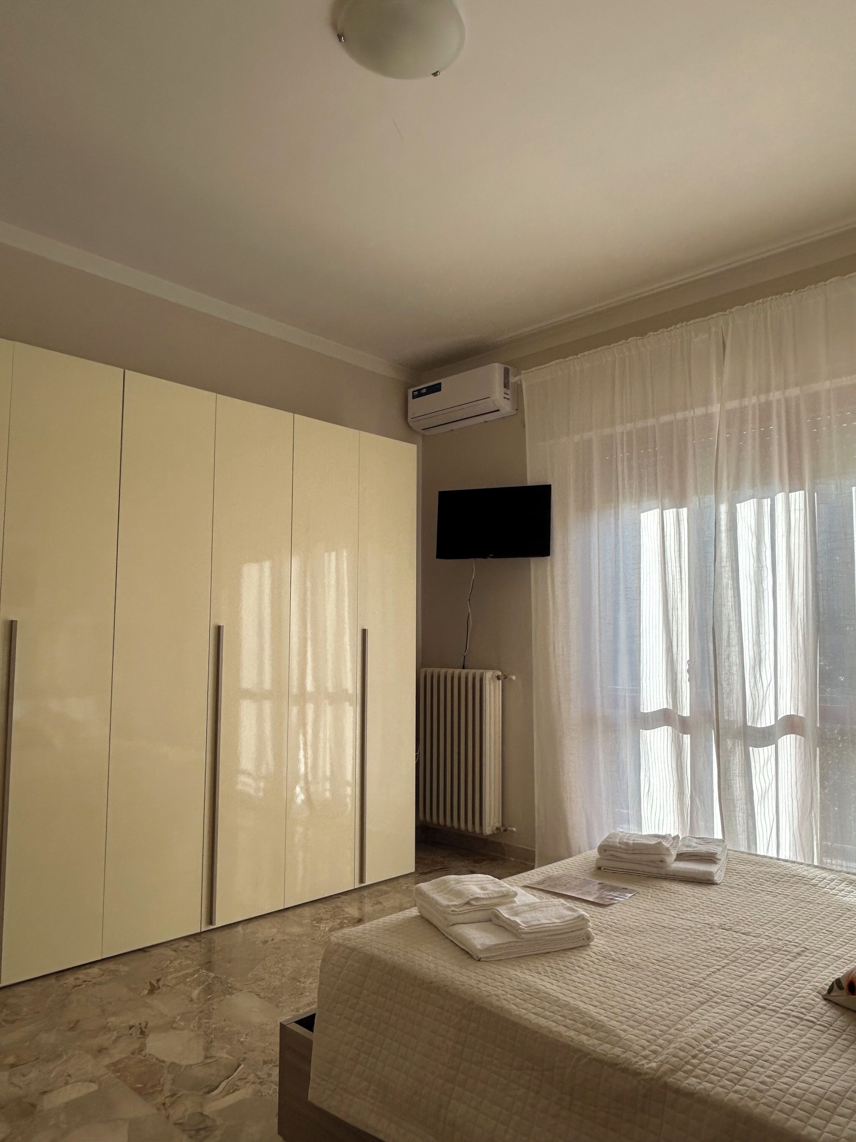 A bedroom with a bed, a wardrobe, an air conditioning unit, a television, and a radiator.