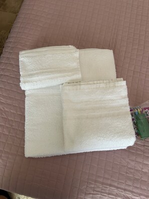 Un lit recouvert d’une couverture rose matelassée et agrémenté de serviettes blanches soigneusement pliées.