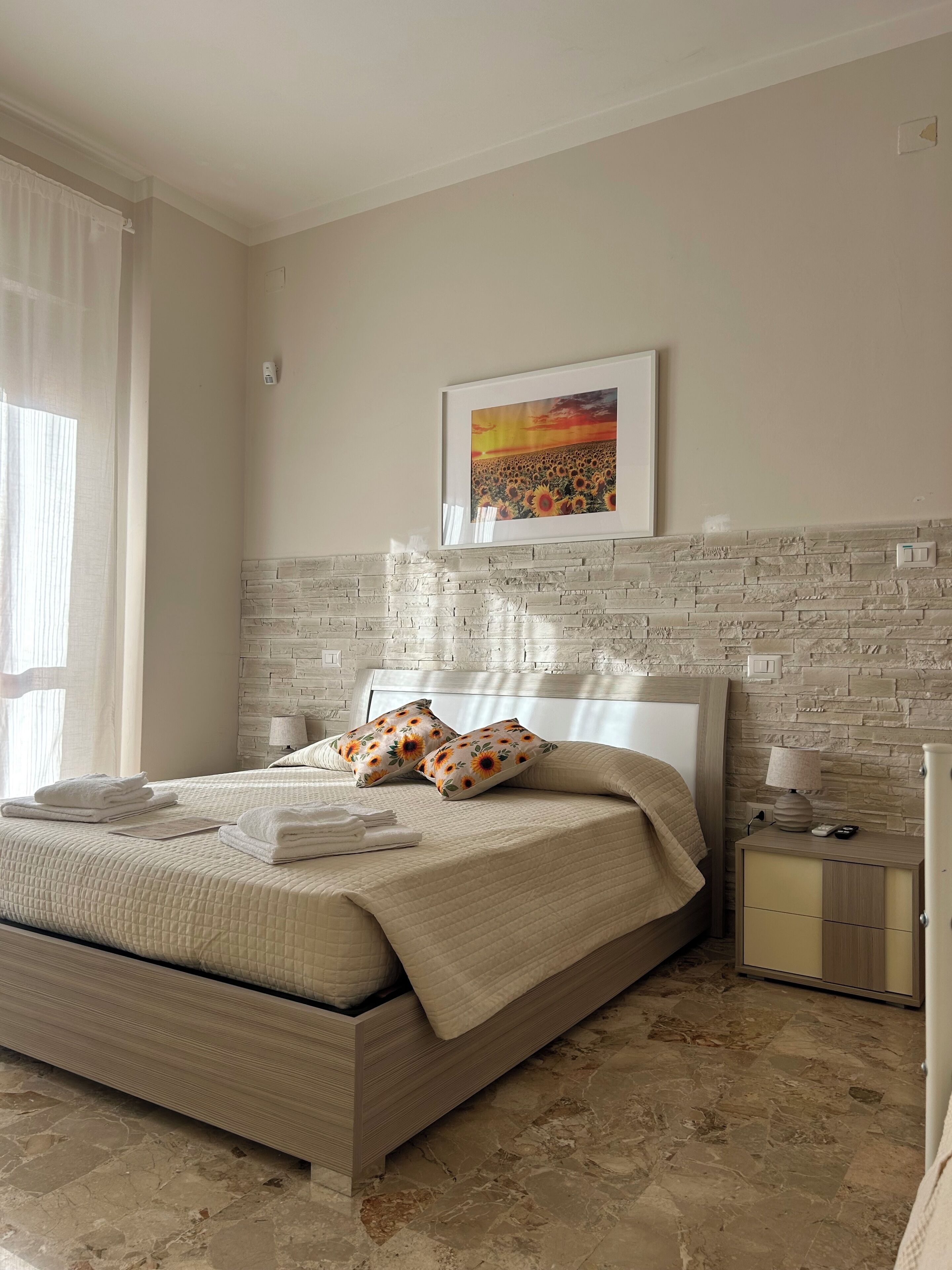 A bedroom with a bed, a nightstand, a lamp, a framed picture on the wall, and a window with curtains.