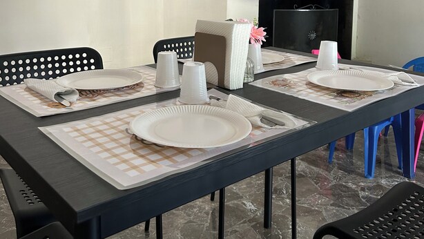Un comedor con una mesa dispuesta para cuatro personas, sillas, un reloj y una estantería con adornos.