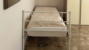 Habitación pequeña con cama individual, estructura de metal, colchón sencillo y armario con puerta.
