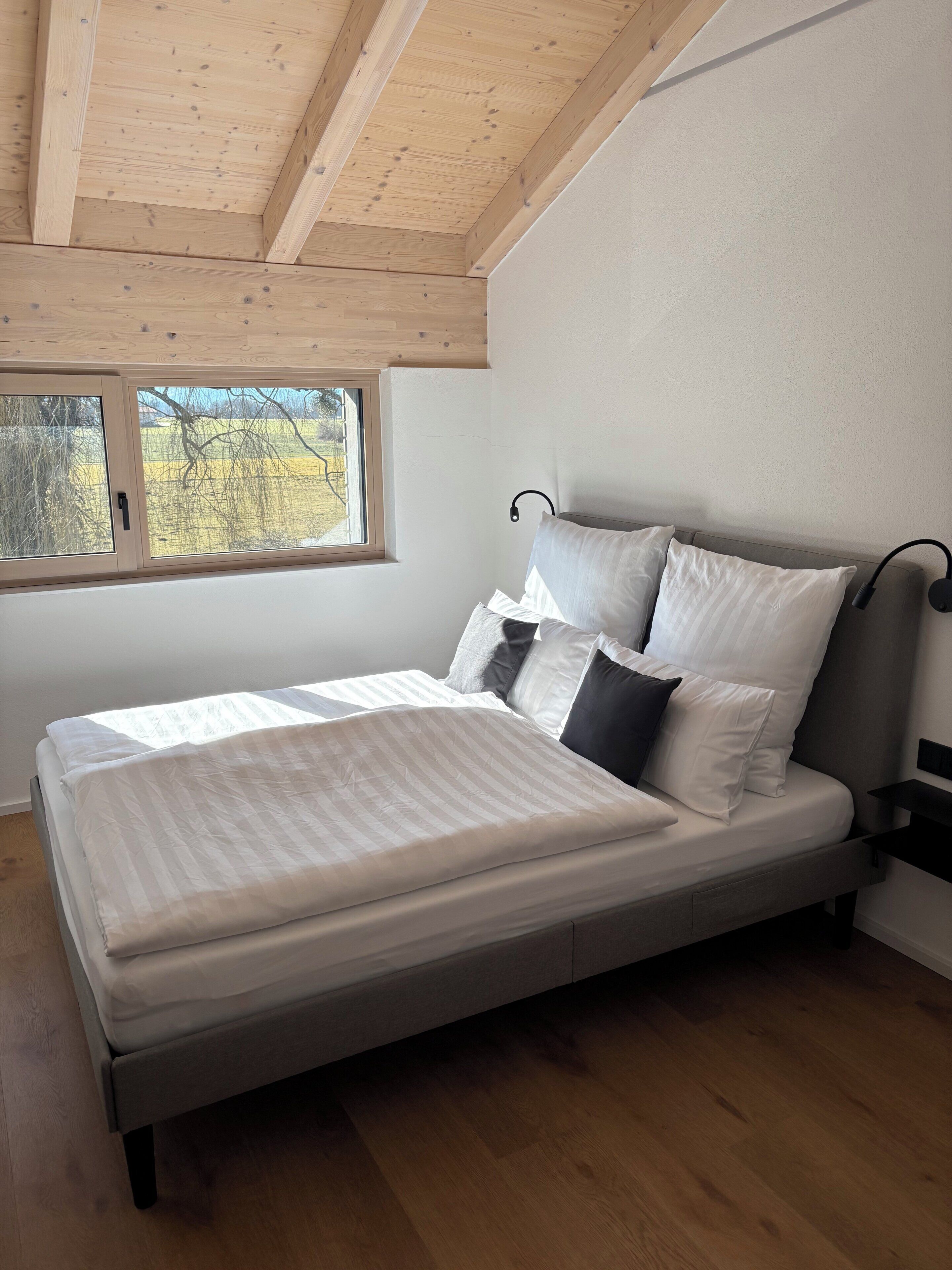 Quarto com uma cama, uma janela e teto de madeira.