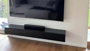 A flat-screen TV mounted on a white wall with a black stand below it. - Mountain Ranges Around Lake Chiemsee (Übersee)