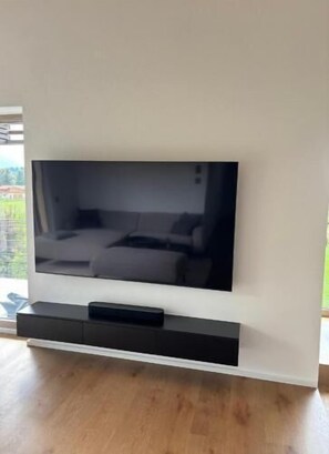 Ein Flachbildfernseher an einer weißen Wand, darunter eine schwarze Halterung.