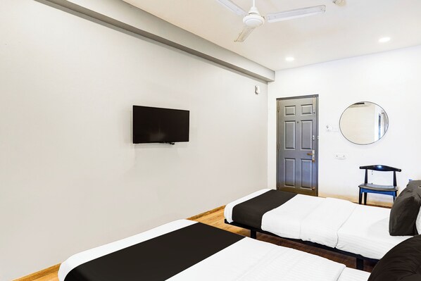A hotel room with two beds, a television, a door, a mirror, and a ceiling fan.