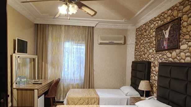 Ein Hotelzimmer mit zwei Betten, einem Schreibtisch, einem Stuhl, einem Fernseher und einem Deckenventilator.