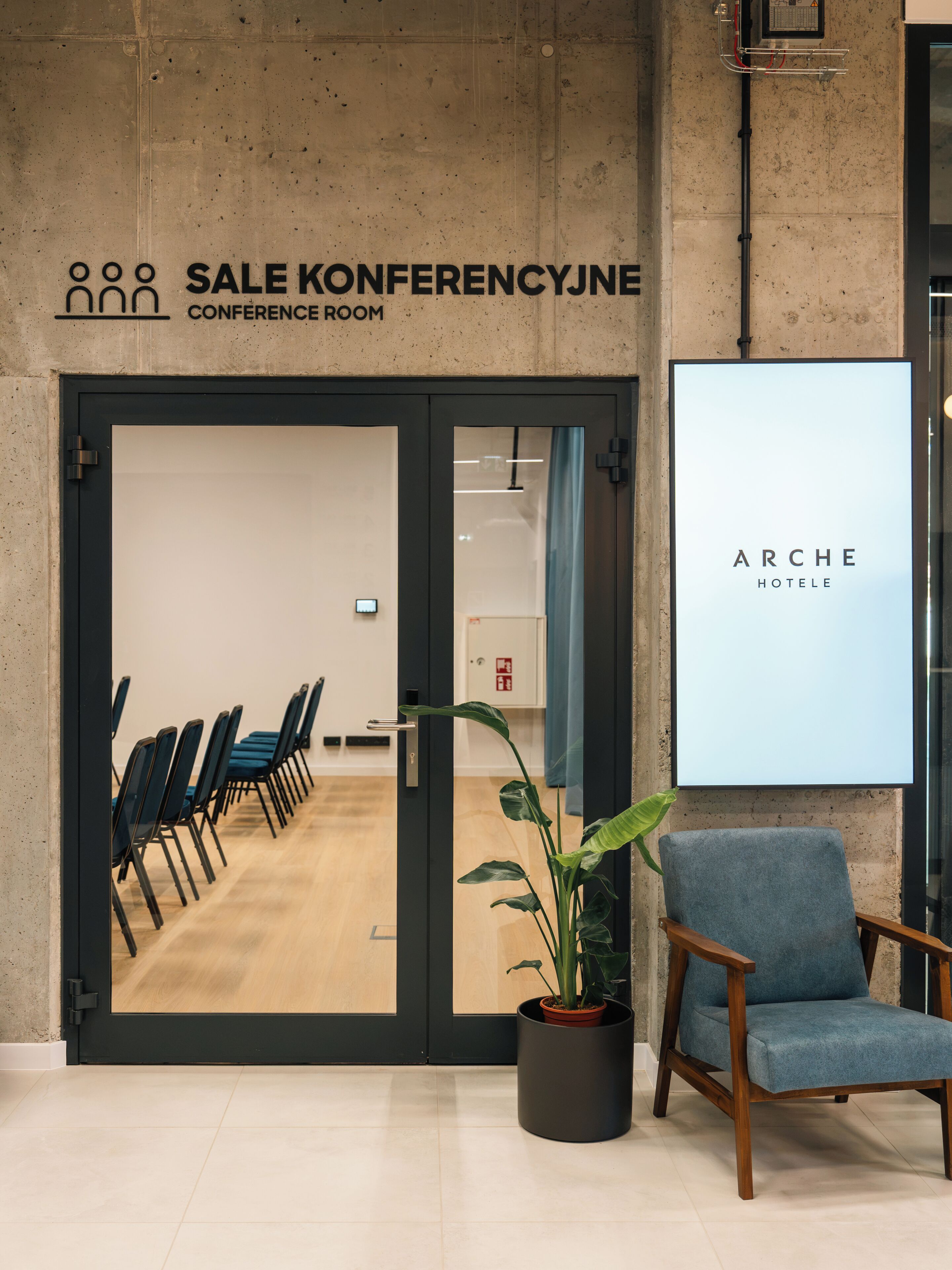 A conference room with a sign indicating it's for sale, a potted plant, and a blue chair.