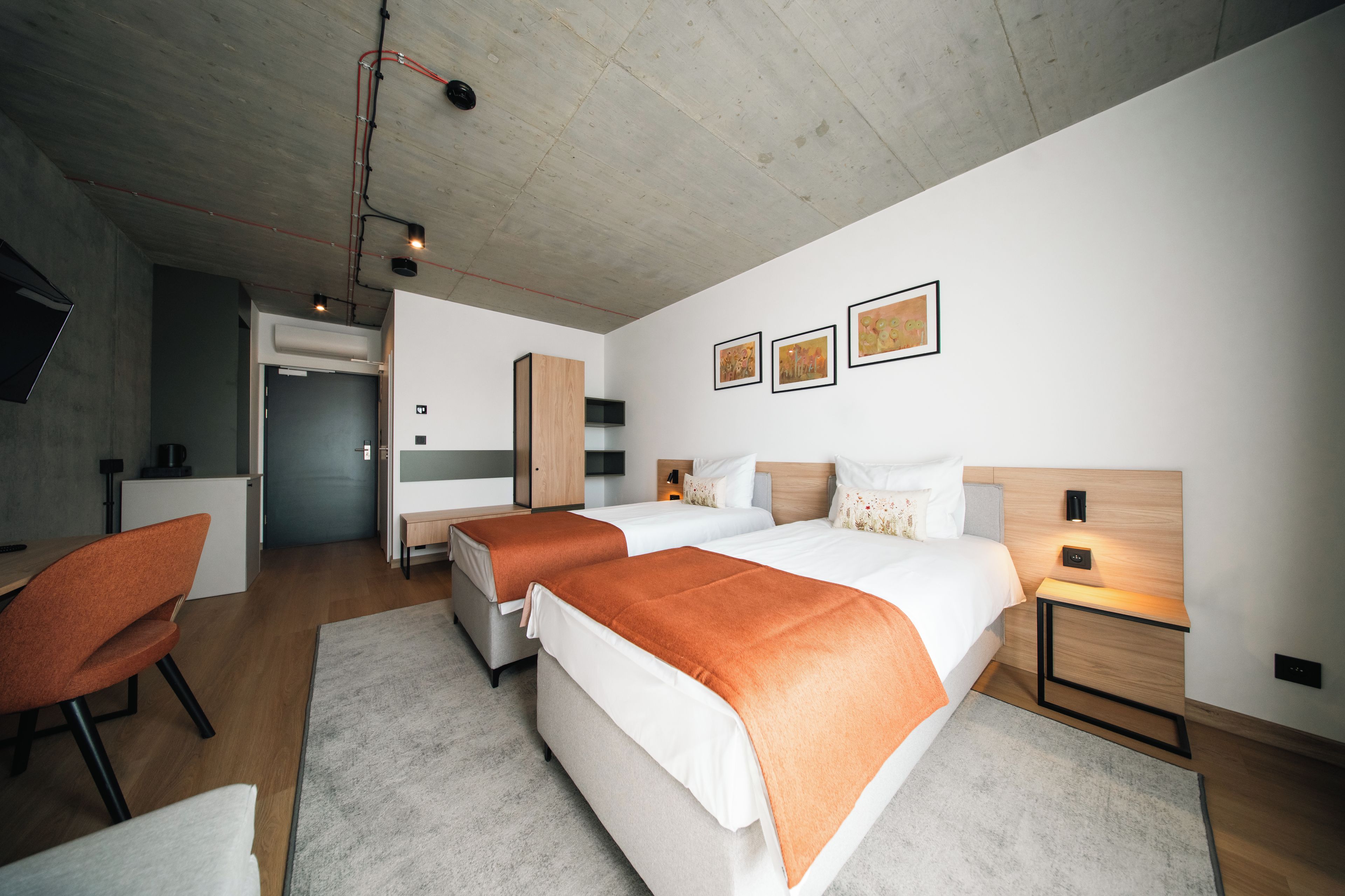 Una habitación de hotel moderna con dos camas, un escritorio, una silla y una obra de arte en la pared.
