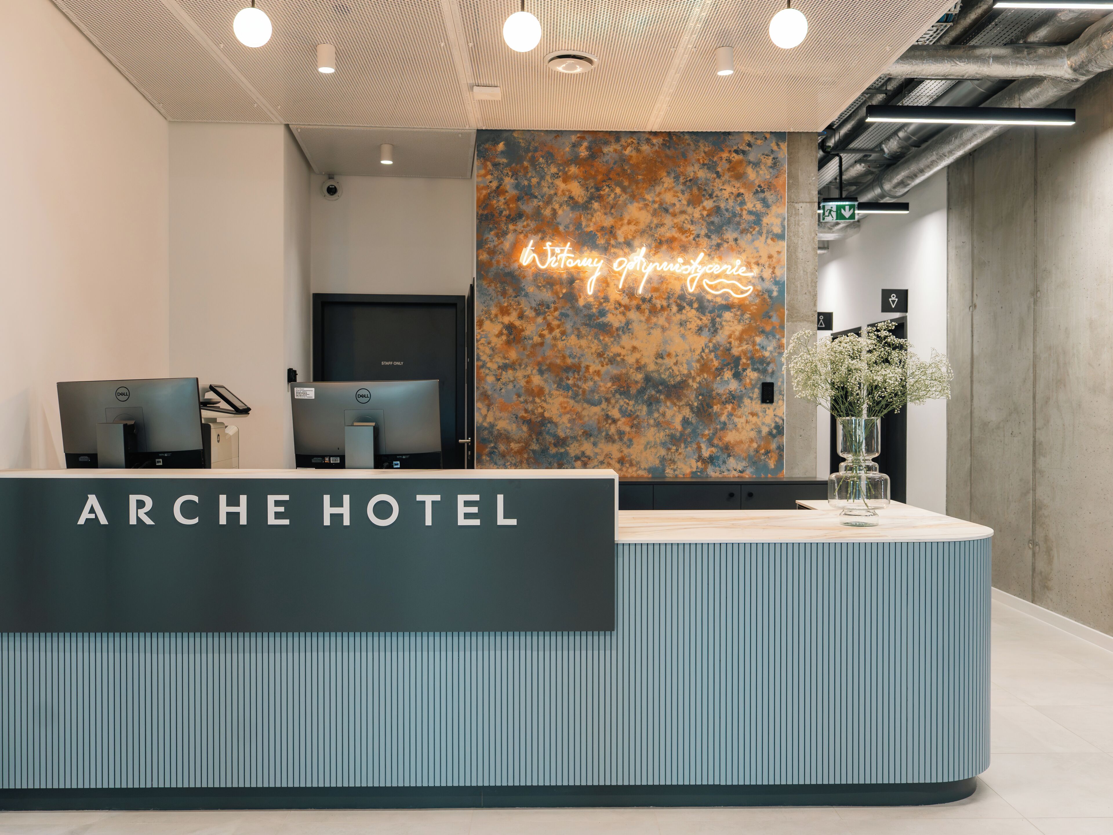 Ein Hotelrezeptionsschalter mit modernem Design, eine Neonreklame und eine Vase mit Blumen.