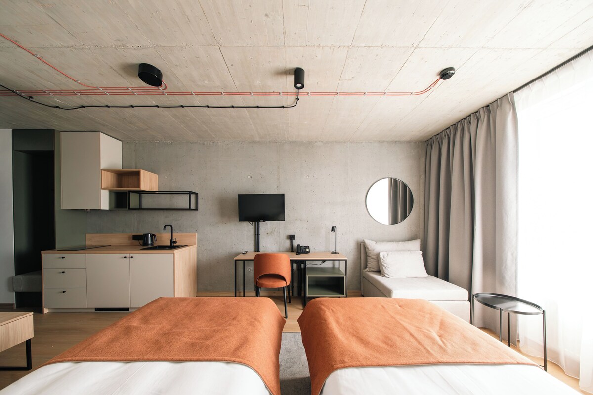 Quarto de hotel com duas camas, uma escrivaninha, uma cadeira, uma televisão e um espelho.