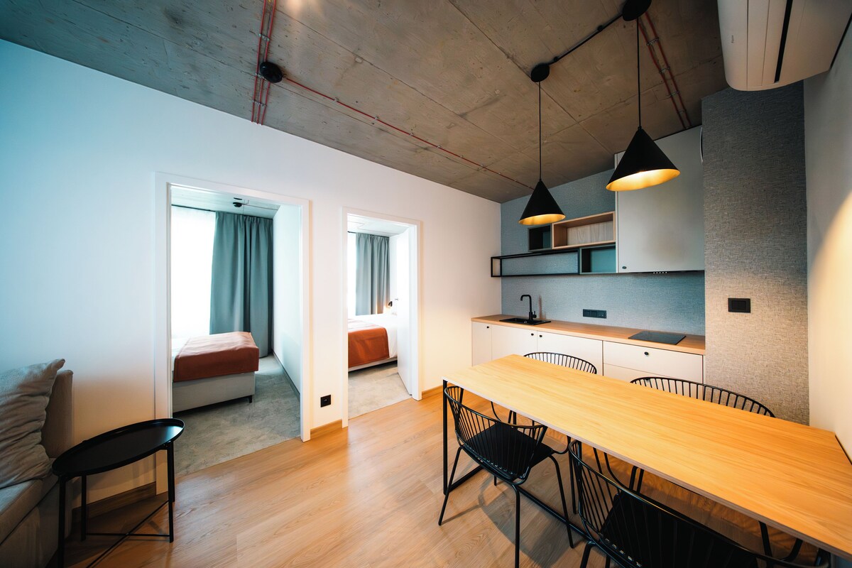 Cozinha moderna com mesa e cadeiras de madeira, forno embutido e luminária pendente.