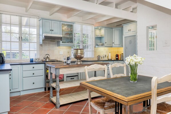 A kitchen with light blue cabinets, a wooden dining table, and a vase of flowers. - The Cockpit (Franschhoek)