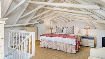A bedroom with a sloped ceiling, a bed with a red and white bedspread, two bedside lamps, a nightstand, and a crib.