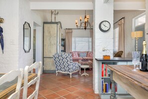 A cozy living room with a patterned armchair, a sofa, and a dining area with a wooden table and books. - The Cockpit (Franschhoek)