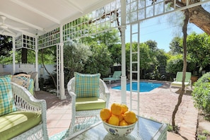 A covered outdoor area with wicker furniture, a pool, and a bowl of fruit. - The Cockpit (Franschhoek)