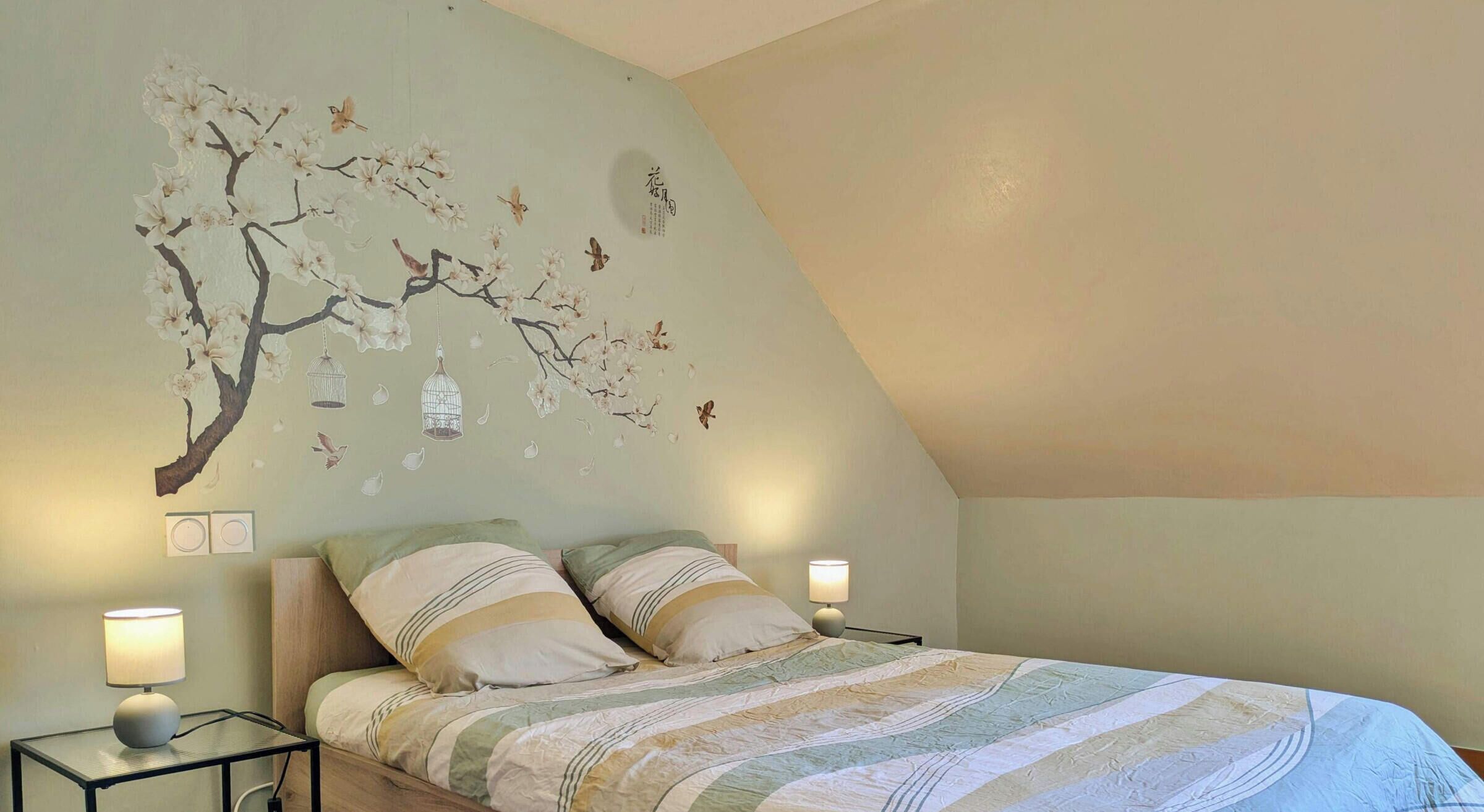 Une chambre à coucher avec un lit, deux tables de chevet, une fresque murale et un plafond en pente.