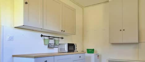 Cozinha com armários brancos, micro-ondas, frigorífico pequeno e radiador.