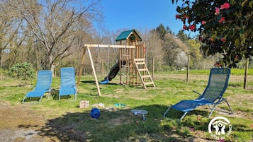Une aire de jeux avec des balançoires et un toboggan, entourée d’herbe et d’arbres.