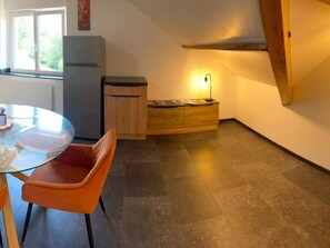 A compact kitchen with a refrigerator, wooden cabinets, a dining table with chairs, and a window with a view of greenery. - Bright apartment on the forest edge - 2 guests (Hadol)