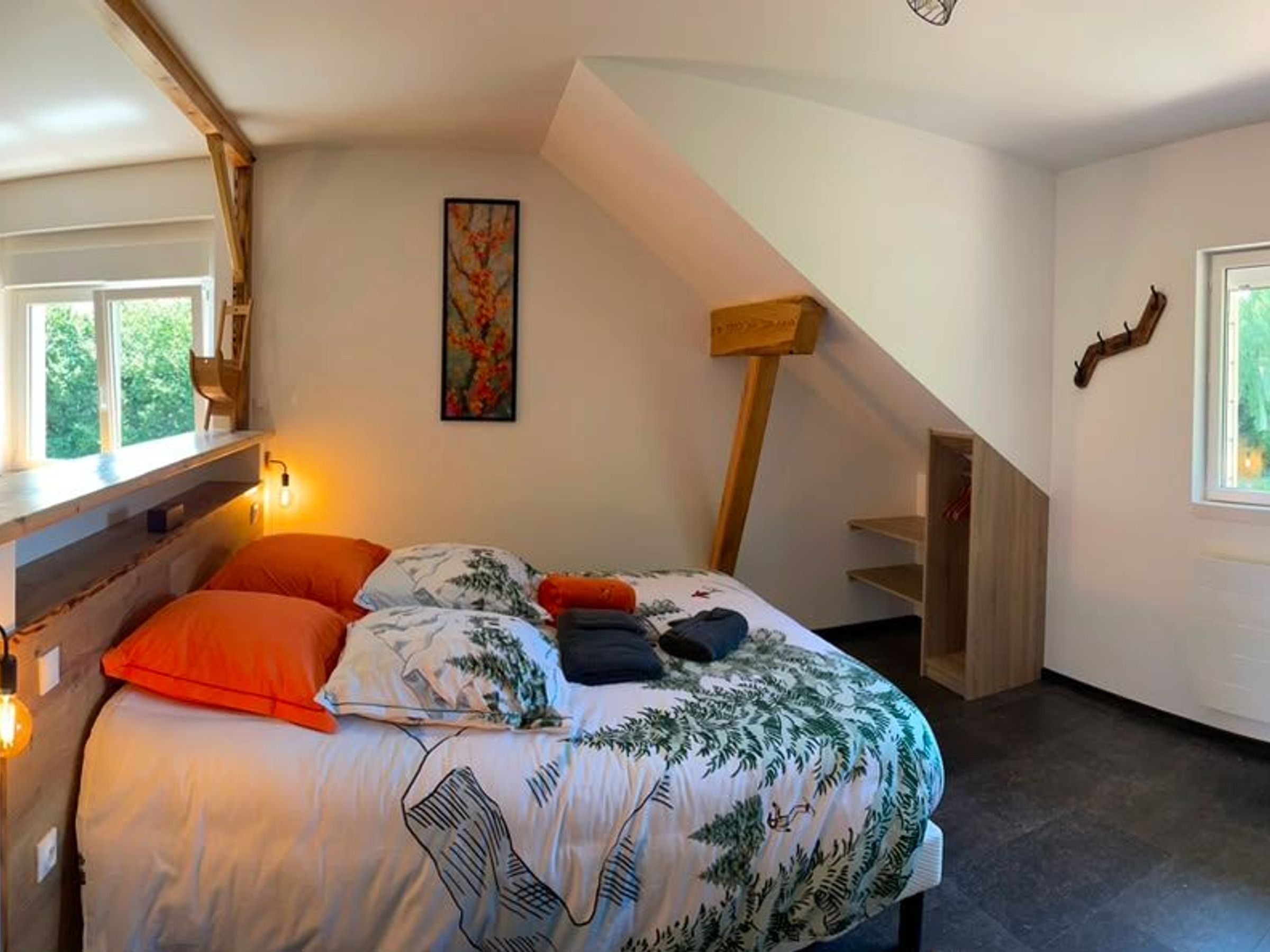 A bedroom with a bed, a painting, a wooden staircase, and a window.