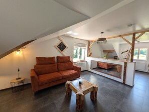 A loft-style room with a sloped ceiling, a brown sofa, a wooden coffee table, and a large mirror reflecting the room. - Bright apartment on the forest edge - 2 guests (Hadol)
