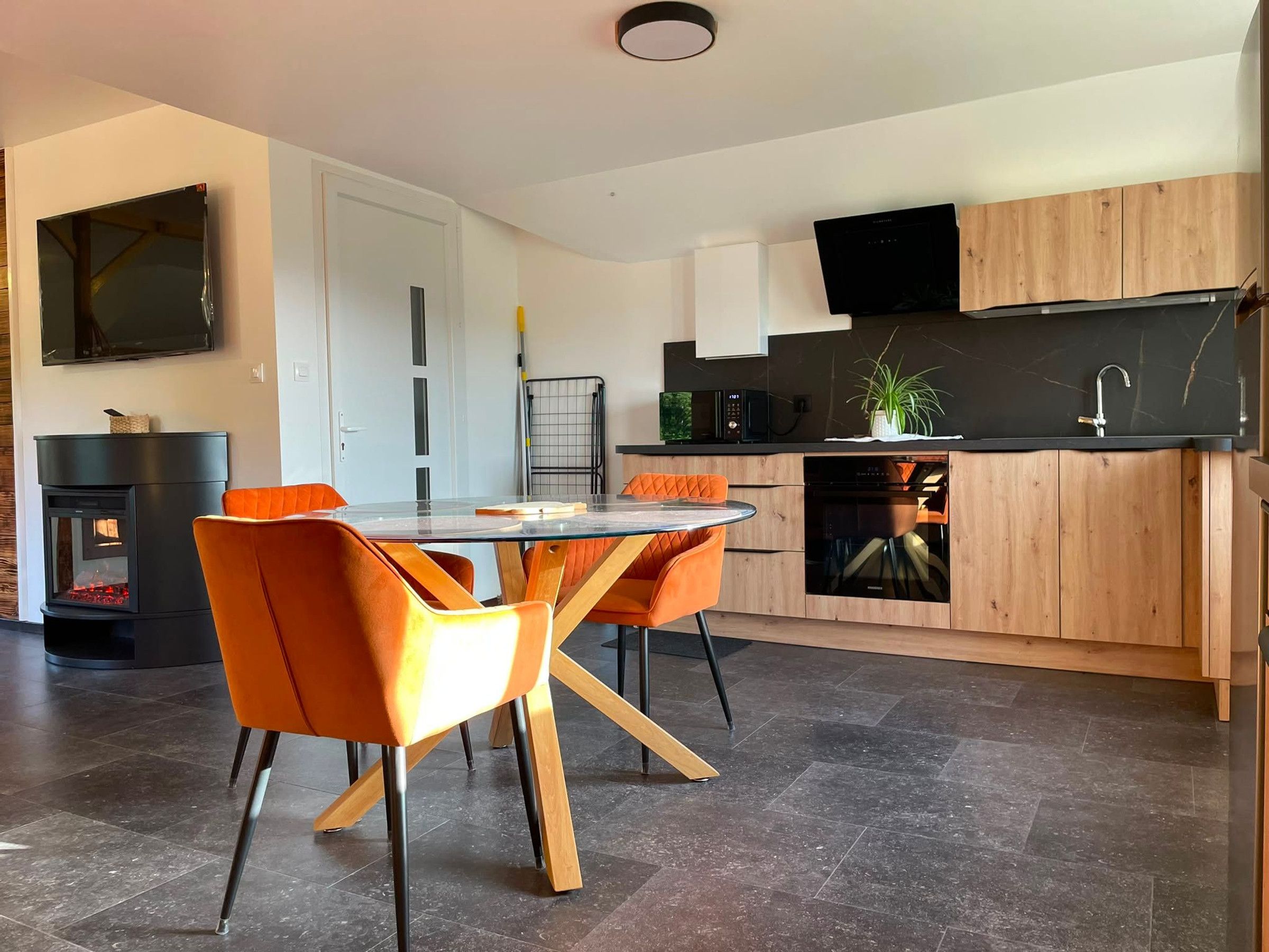 Eine moderne Küche mit Essbereich, ausgestattet mit einem runden Glastisch, orangefarbenen Stühlen und einem eingebauten Backofen.
