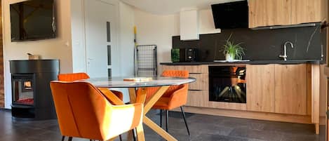 Eine moderne Küche mit Essbereich, ausgestattet mit einem runden Glastisch, orangefarbenen Stühlen und einem eingebauten Backofen.