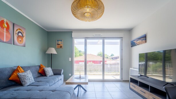 Ein modernes Wohnzimmer mit einem grauen Sofa, einem Flachbildfernseher und einem großen Fenster.
