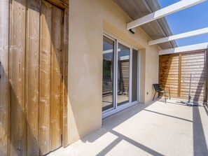 Ein modernes Gebäude mit Holzfassade, großen Schiebeglastüren und einer Terrassenfläche mit einem Metallstuhl.
