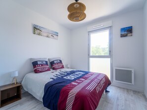 Ein Schlafzimmer mit einem Bett, zwei Kissen, einem Nachttisch, einer Lampe, einem Fenster und einer Wand-Klimaanlage.