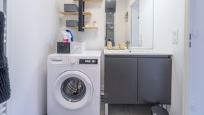 Ein kleines Badezimmer mit Waschmaschine, Waschbecken und Spiegel.